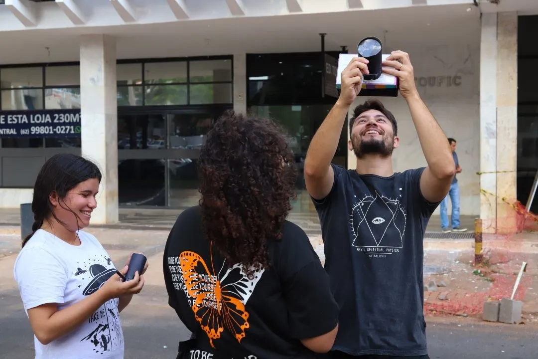 Três jovens em atividade de audiovisual na rua, um deles ergue uma lente para o céu
