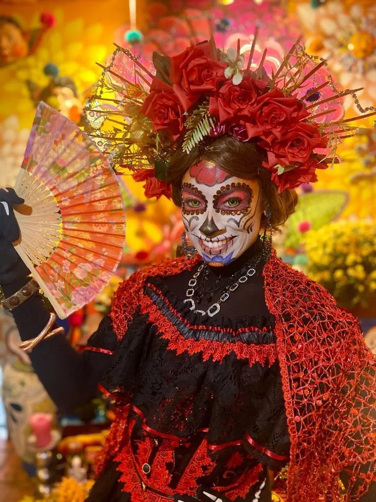 Artista com maquiagem de caveira mexicana, coroa de rosas e leque