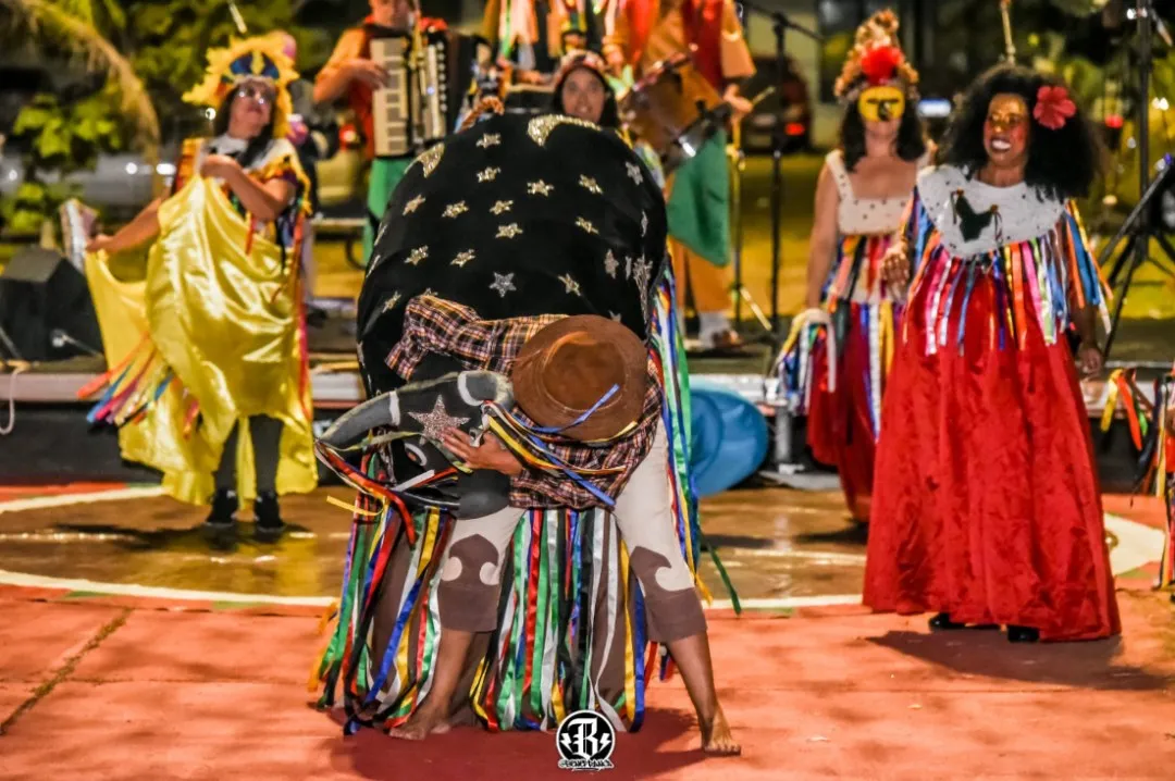 Brincantes de boi com fitas coloridas e chapéus enfeitados em apresentação noturna