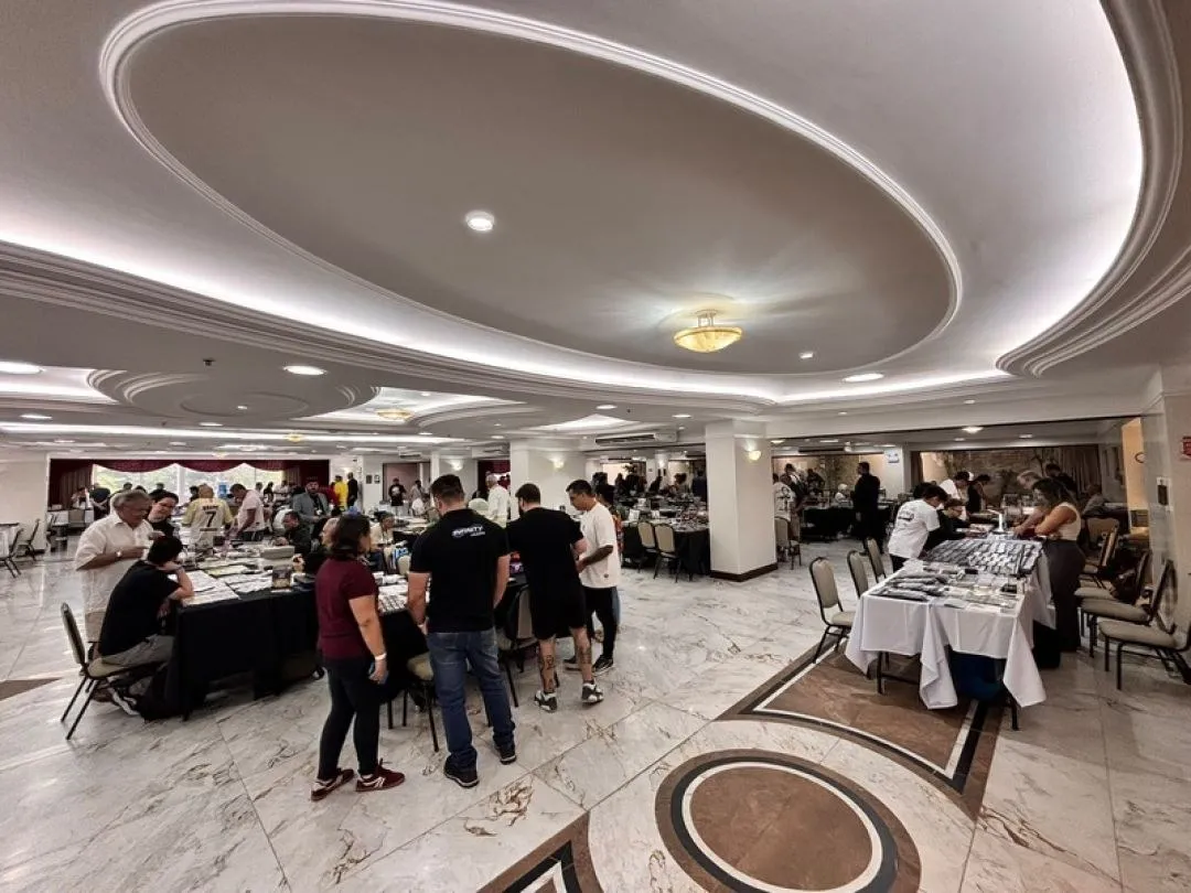 Salão de hotel com mesas de expositores e visitantes em encontro de colecionadores