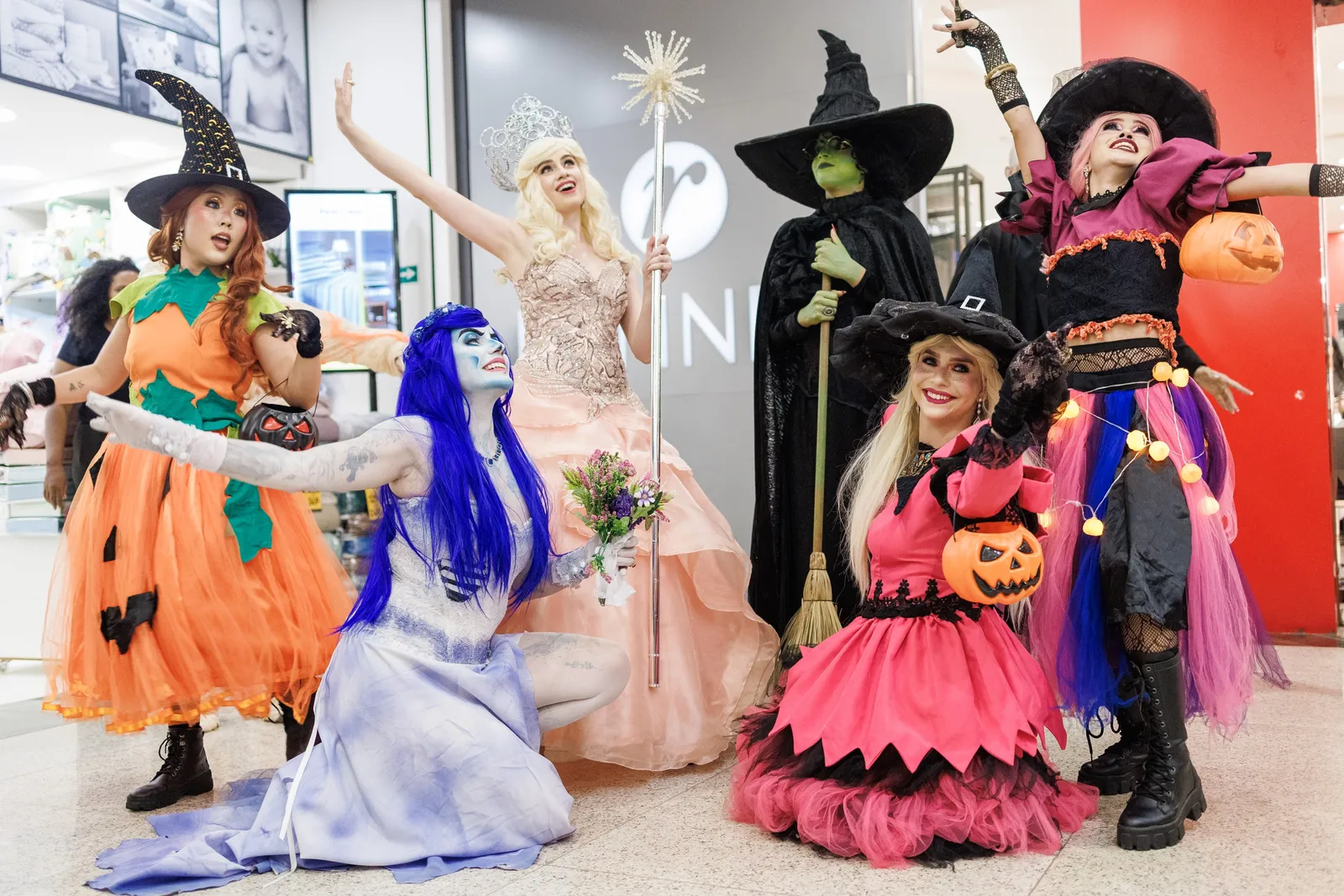 Seis artistas fantasiados de bruxas e personagens de Halloween posam em corredor de shopping